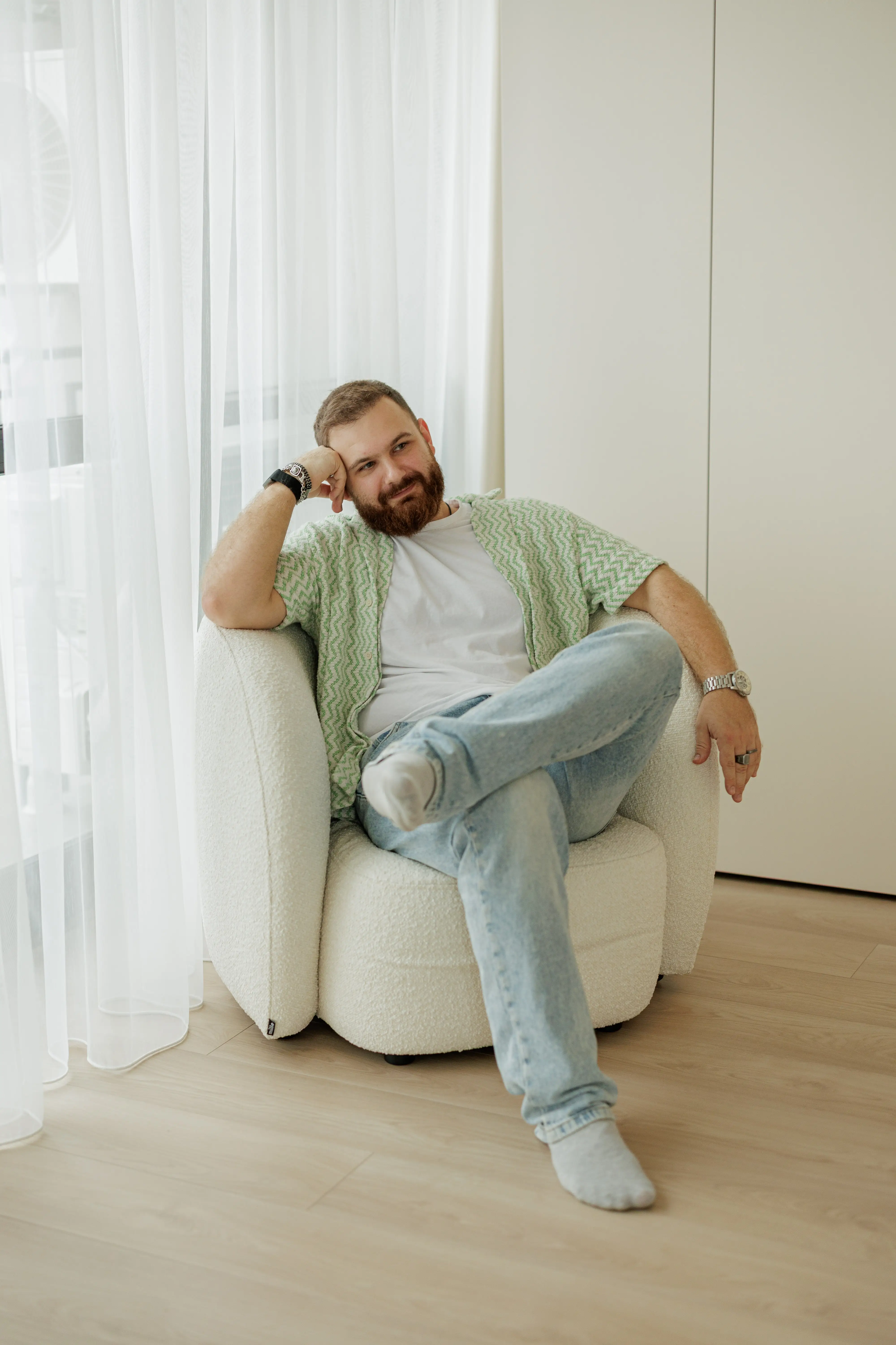A man seated in a cream boucle Nuba armchair in an apartment, hand to his cheek