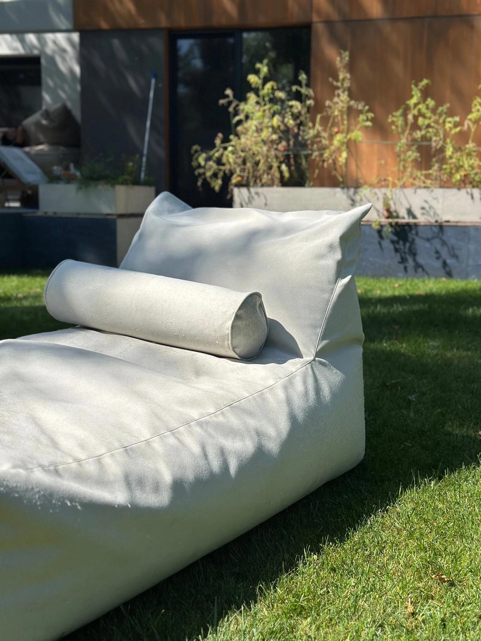 Cream Marolla lounger with bolster, side view on a villa lawn