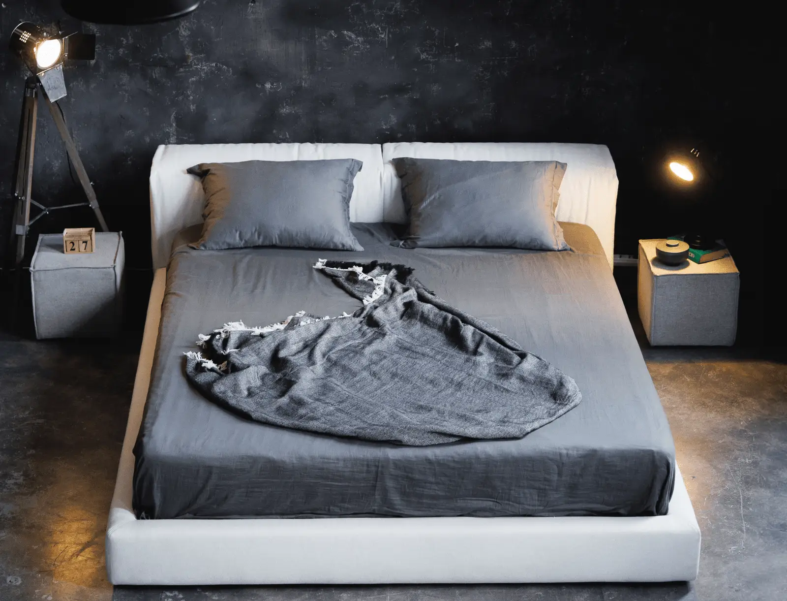 Cream Marmaris in a dark concrete-walled loft with a grey duvet and a photographic light stand on the right