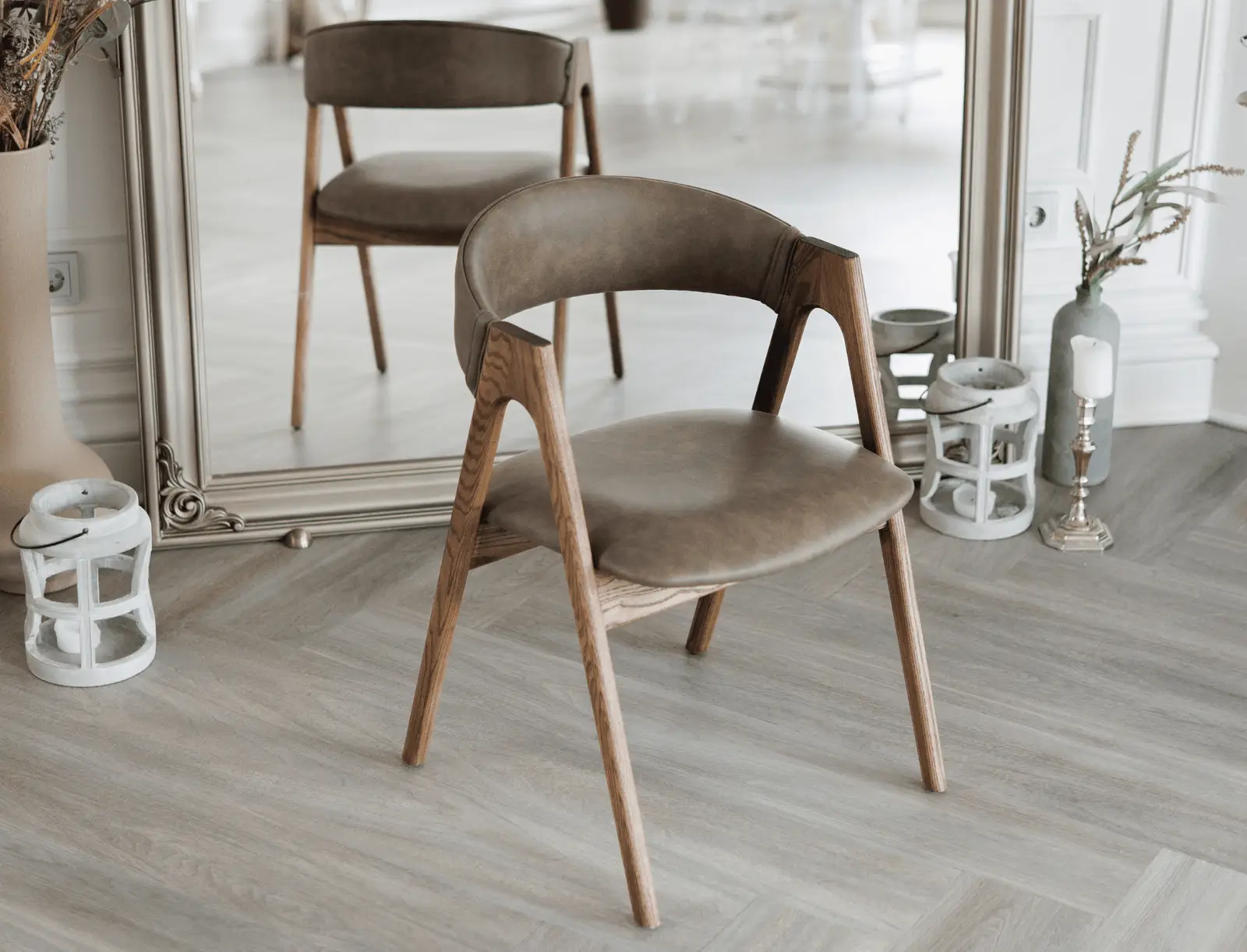 Coffee-brown leather Lain chair on natural-ash frame beside a tall gold-framed mirror with candles