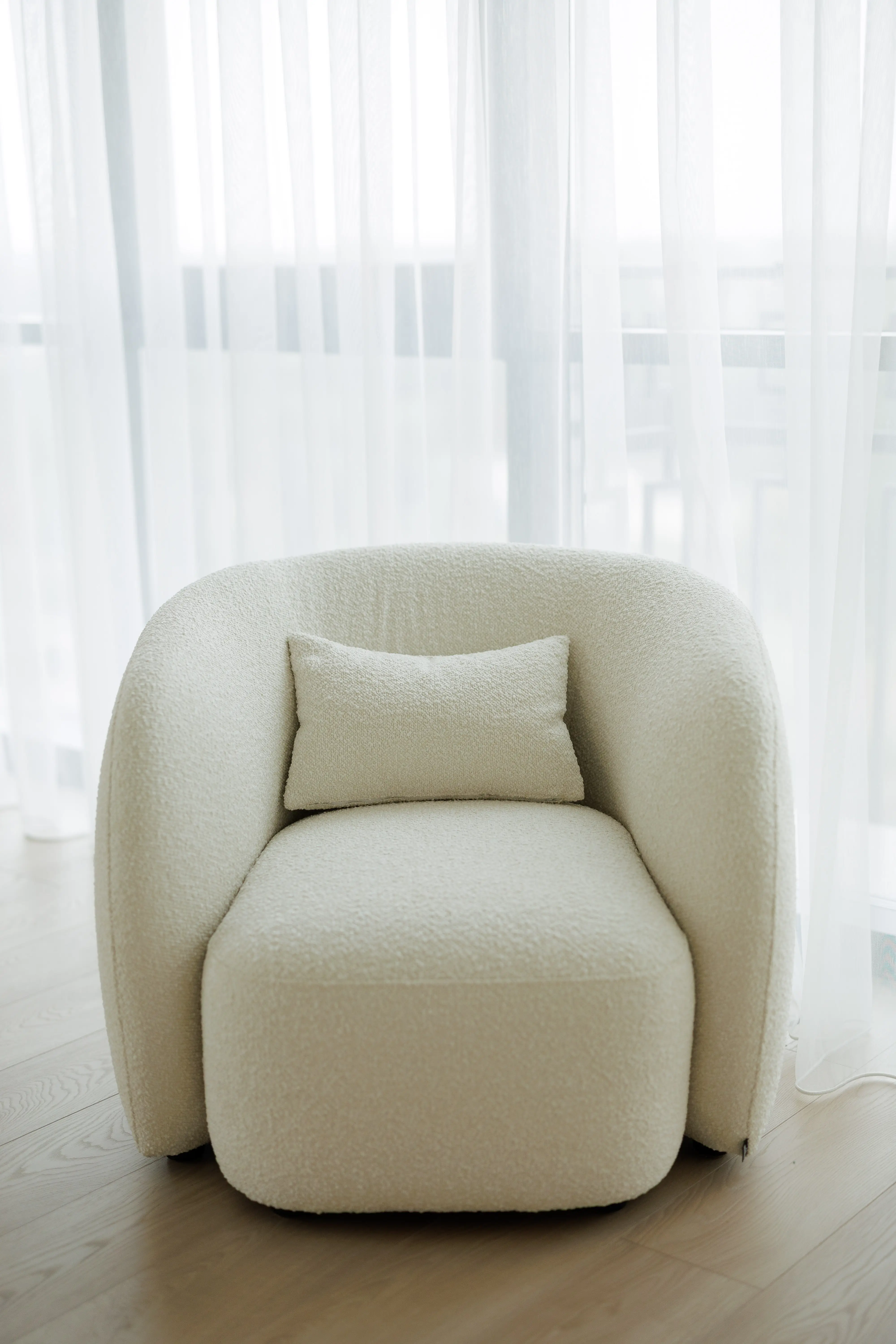 Cream boucle Nuba armchair alone, backlit by sheer white curtains