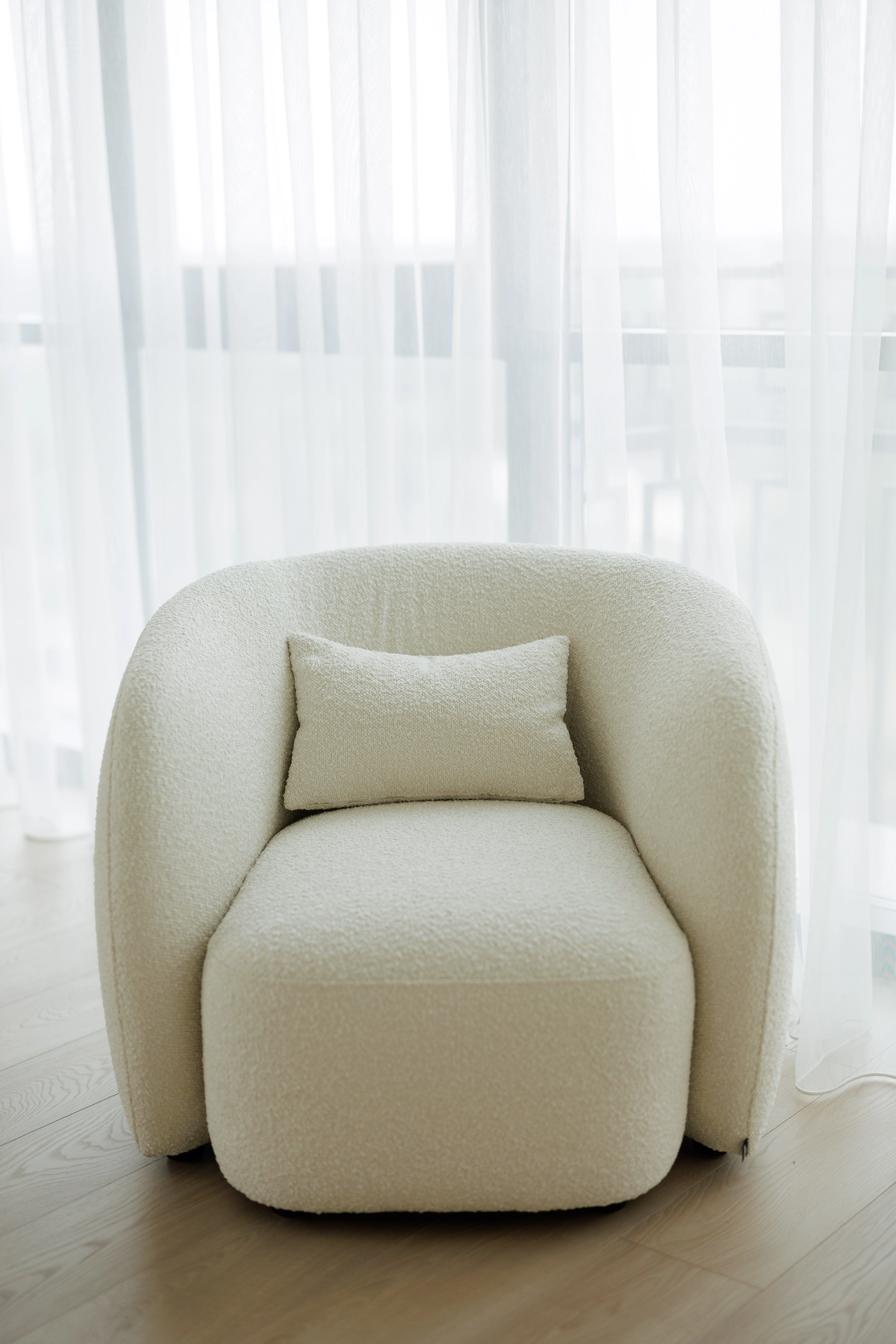 Cream boucle Nuba armchair alone, backlit by sheer white curtains