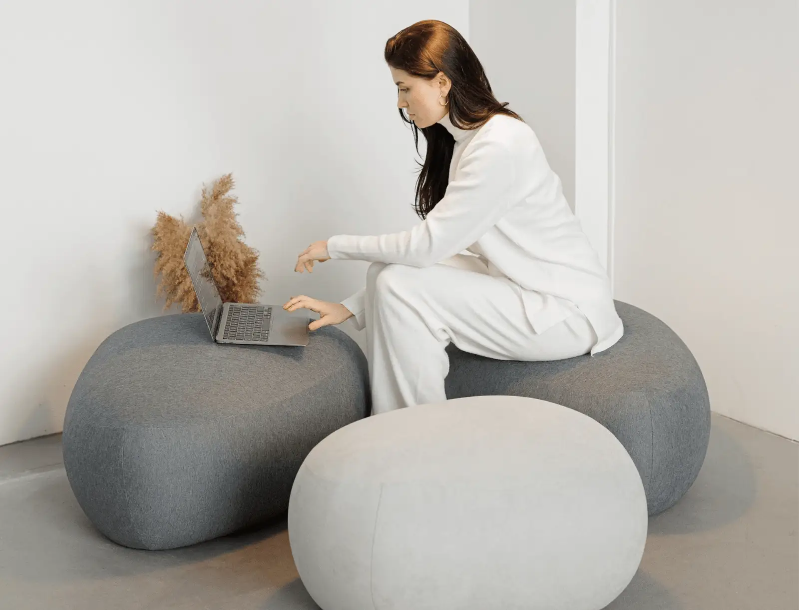 A person seated on a Chios pouf using a laptop in a bright studio