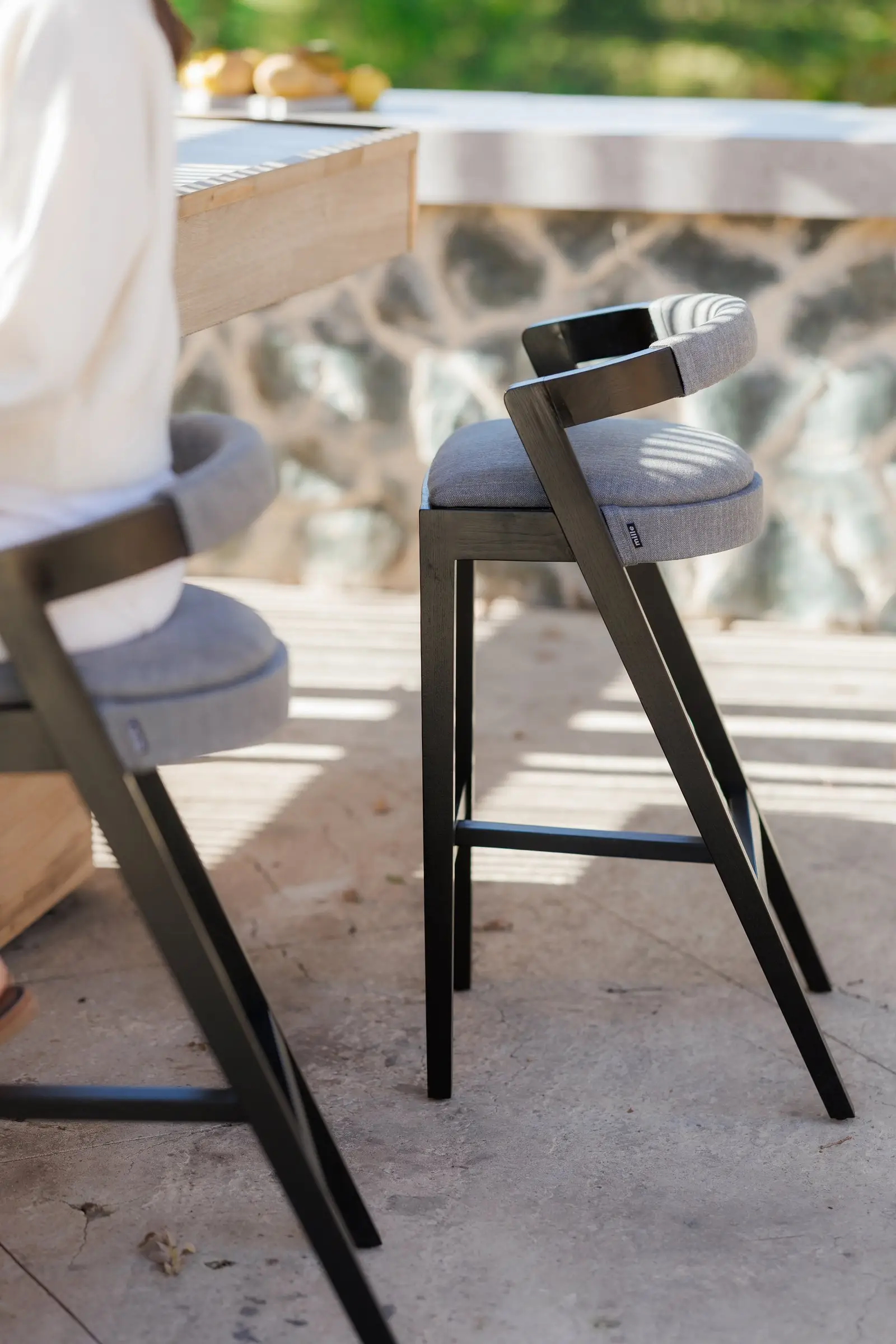 Side angle of a Baffi bar stool at the villa counter showing the black-ash sawhorse frame