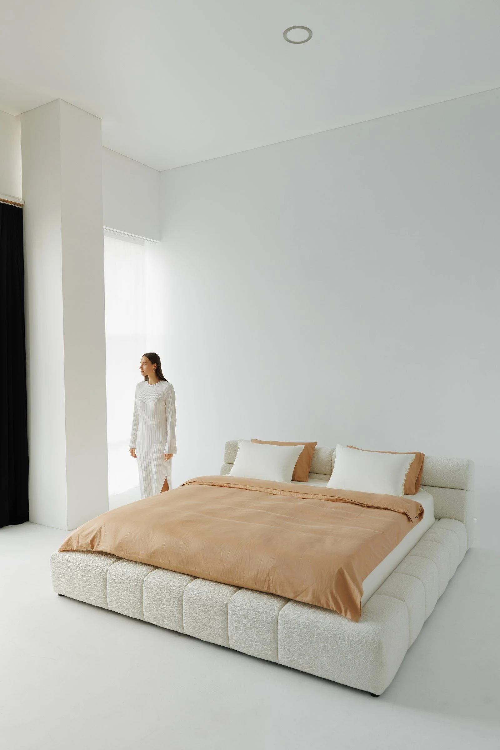 Cream boucle Nao in a bright white room with a model in white ribbed loungewear standing nearby