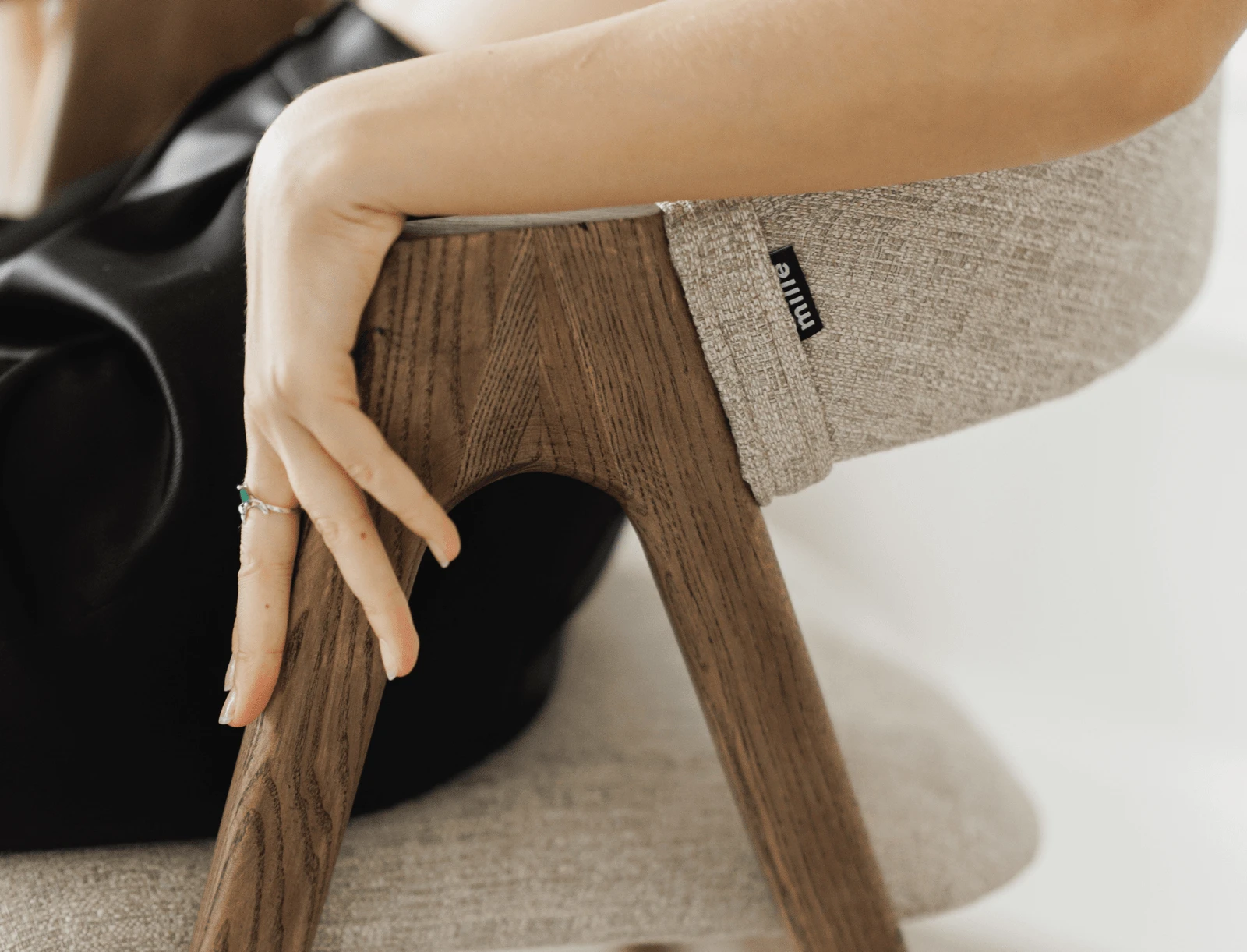 Close detail of the small Mille label on the grey Lain seat with a hand on the ash leg