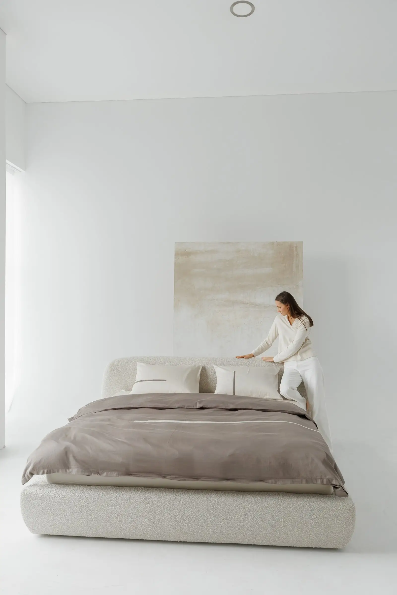 Cream boucle Belagio with a model in cream loungewear tucking a brown linen sheet across the bed