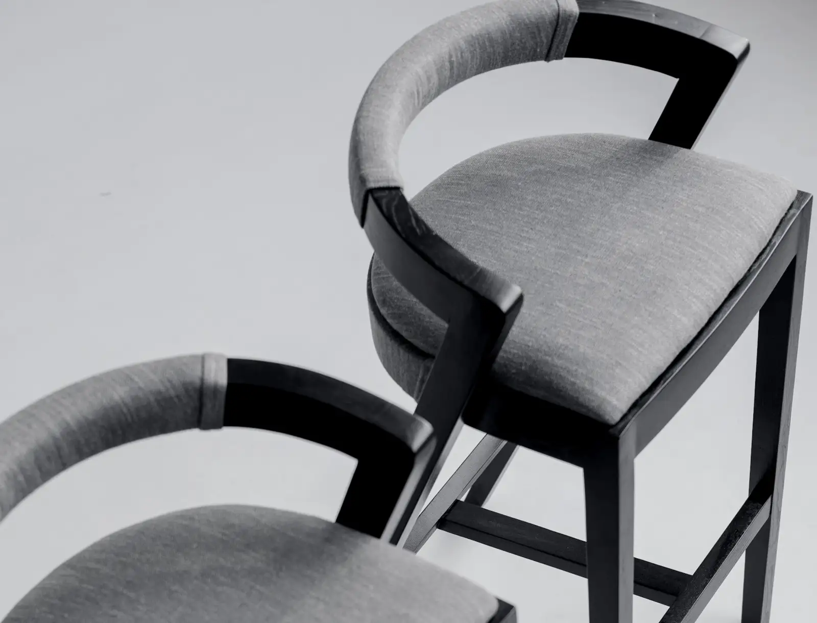 Three-quarter view of the Baffi bar stool in the studio showing the black ash frame and grey upholstered seat