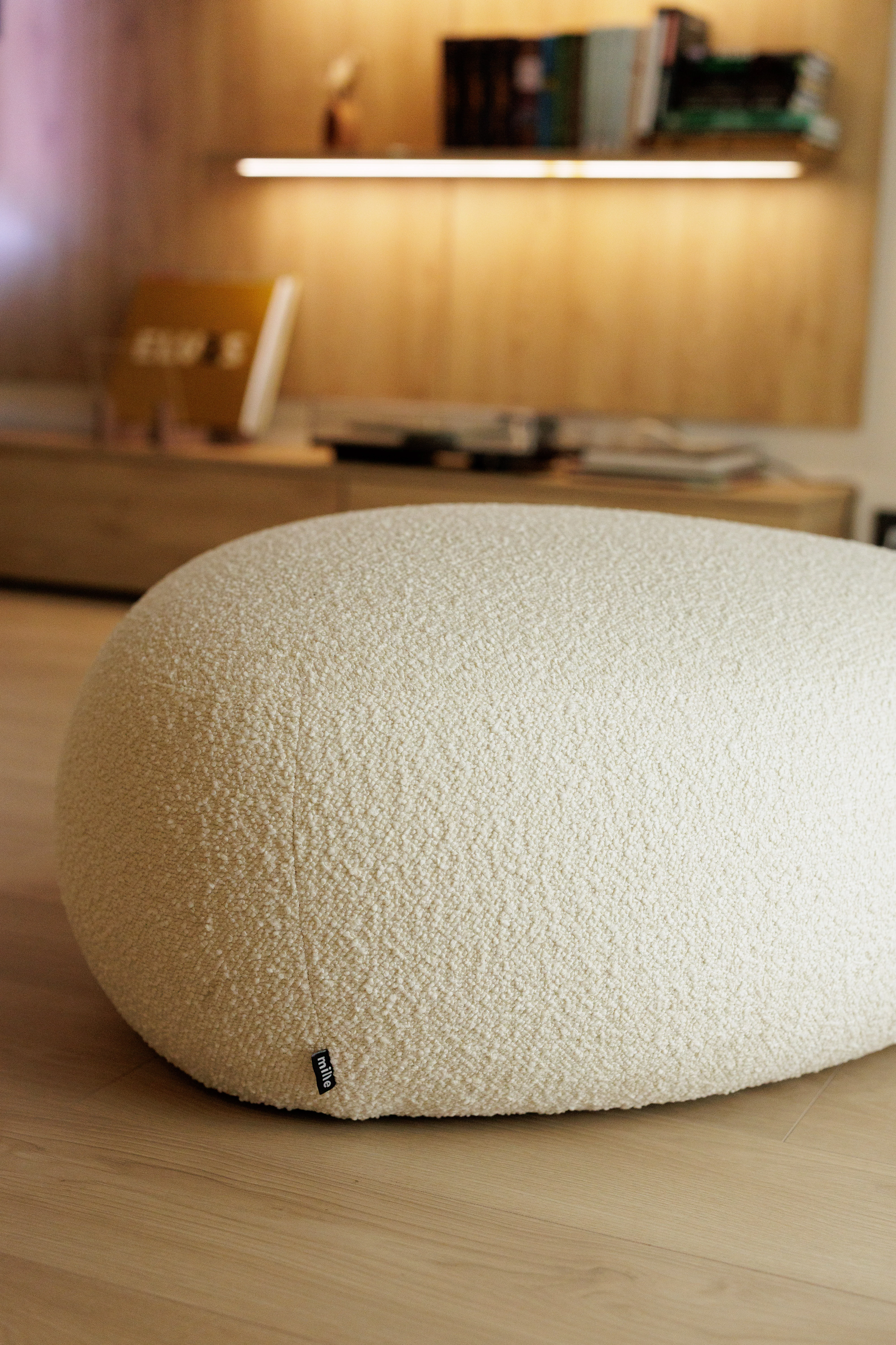 Cream bouclé Chios pouf in a warm room with a lit bookshelf