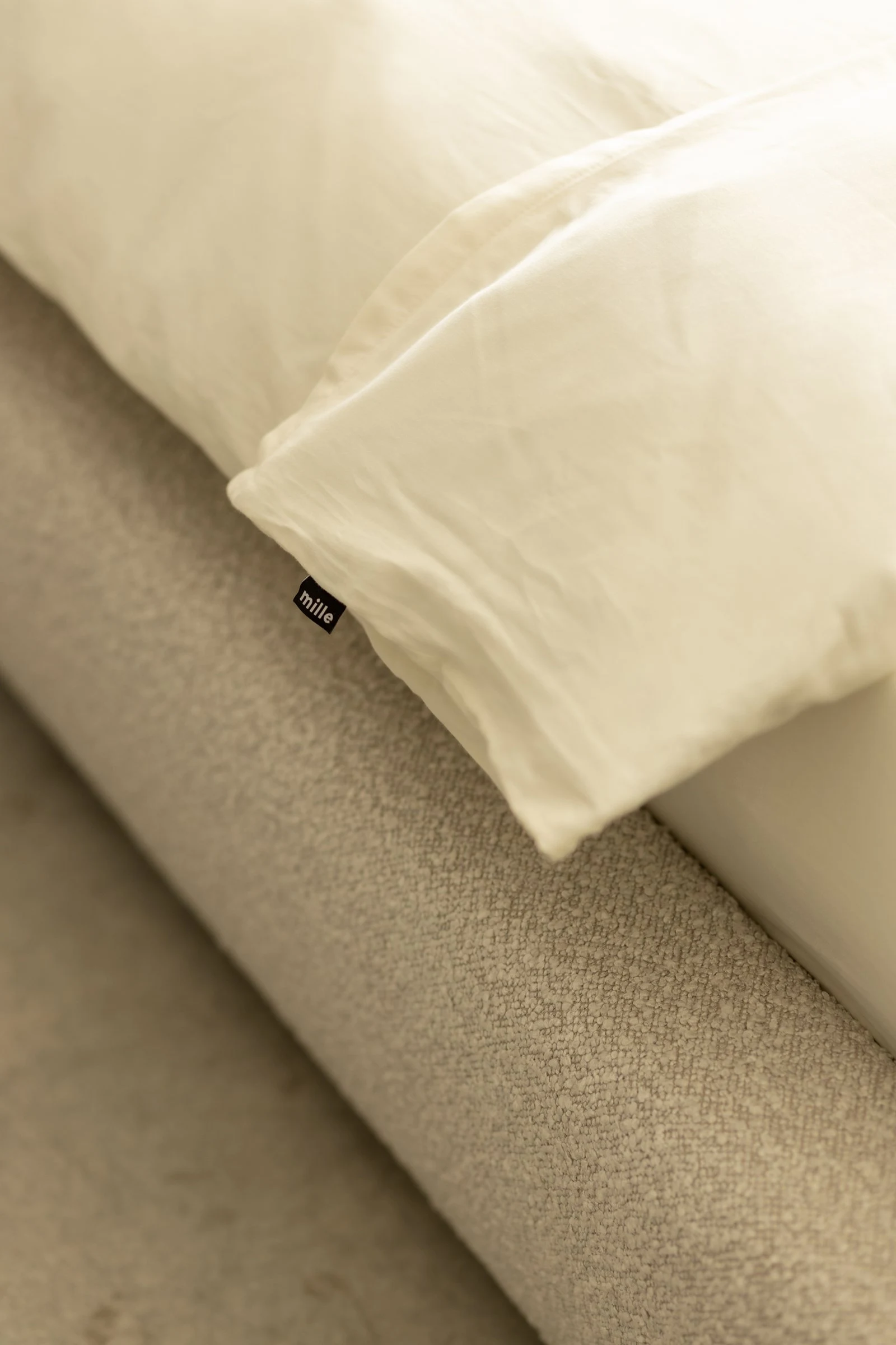 Close detail of a small black Mille label sewn into the boucle seam, with a cream pillow above