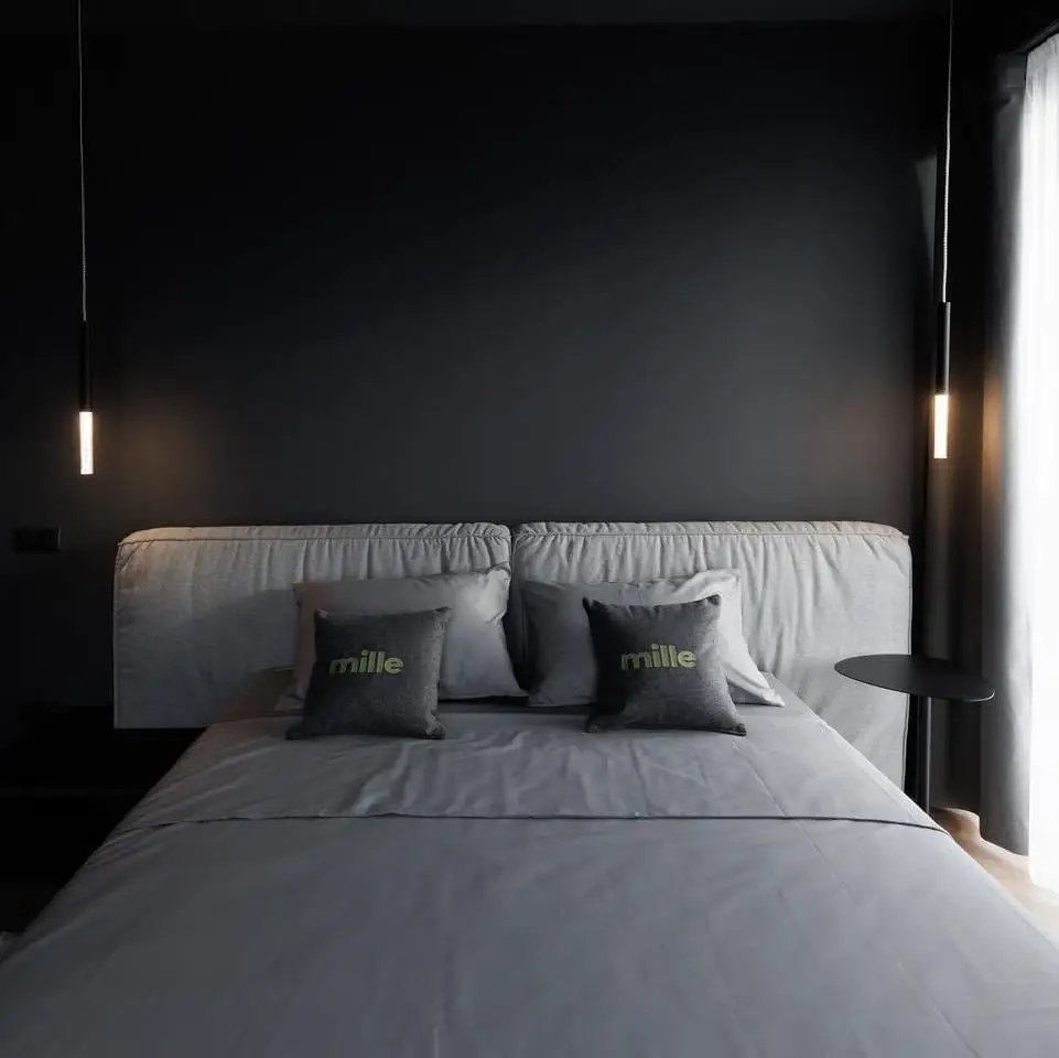 Mid-grey Palermo photographed dead-centered in a dark bedroom with Mille-branded pillows on the bed and tube pendants either side
