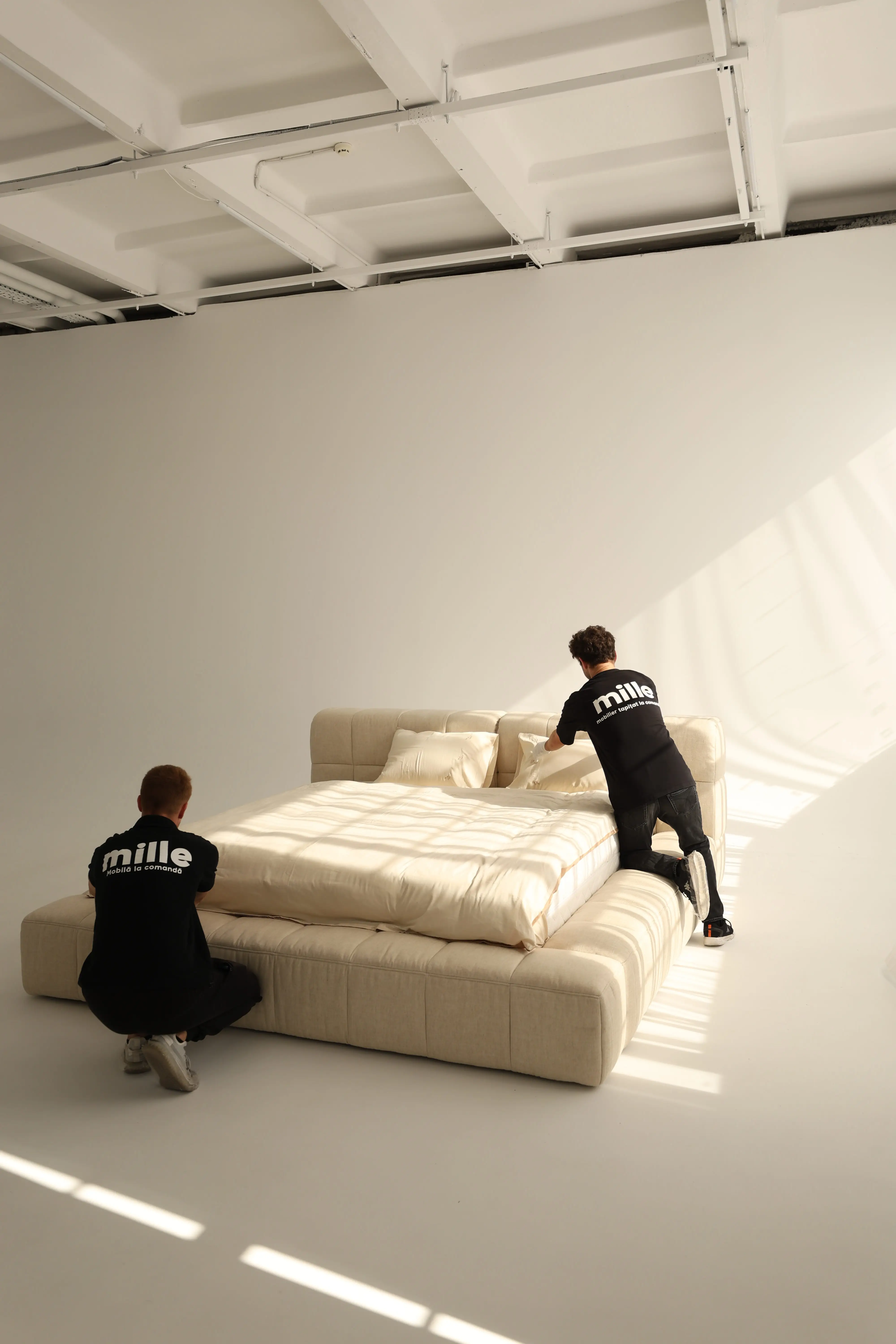 Two Mille technicians making the bed in a bright studio, the cream Nao mid-dress