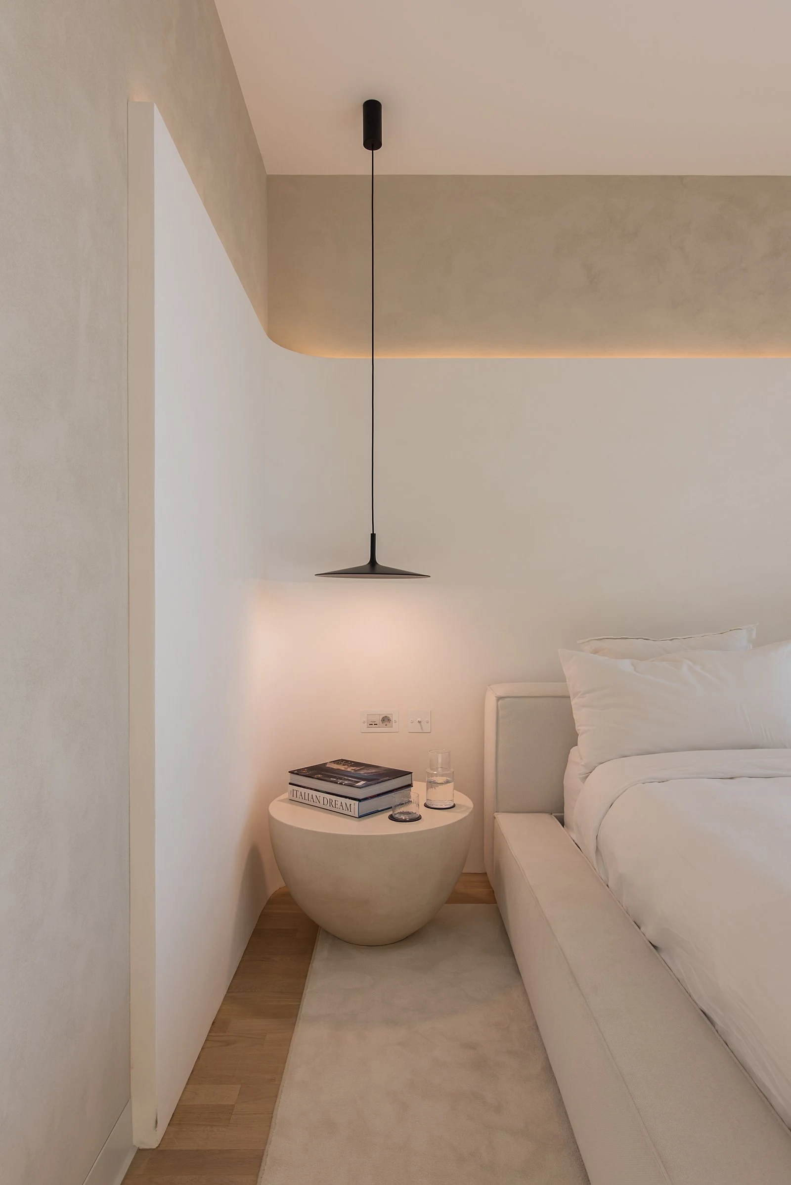 Pebble-shaped concrete side table beside the cream Palermo with an open book and a glass of water on top