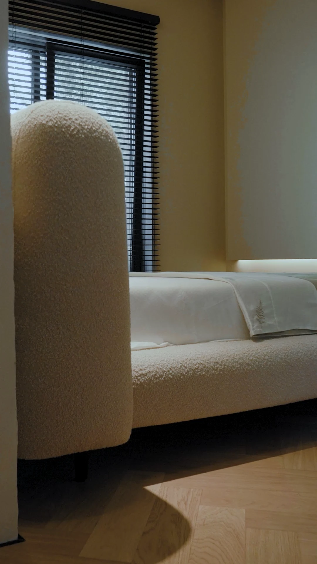 Side view of the Fresco bed seen through a doorway, showing the arched headboard end profile and venetian blinds