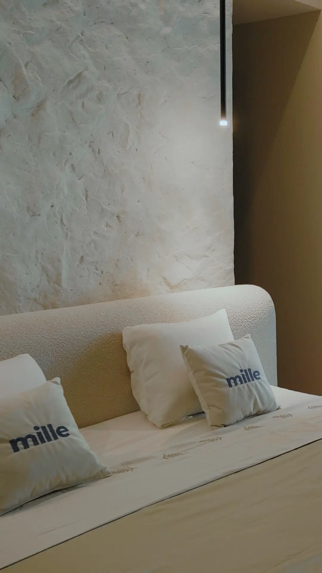 Vertical detail of the cream Fresco arched headboard against a textured plaster wall with Mille pillows in front