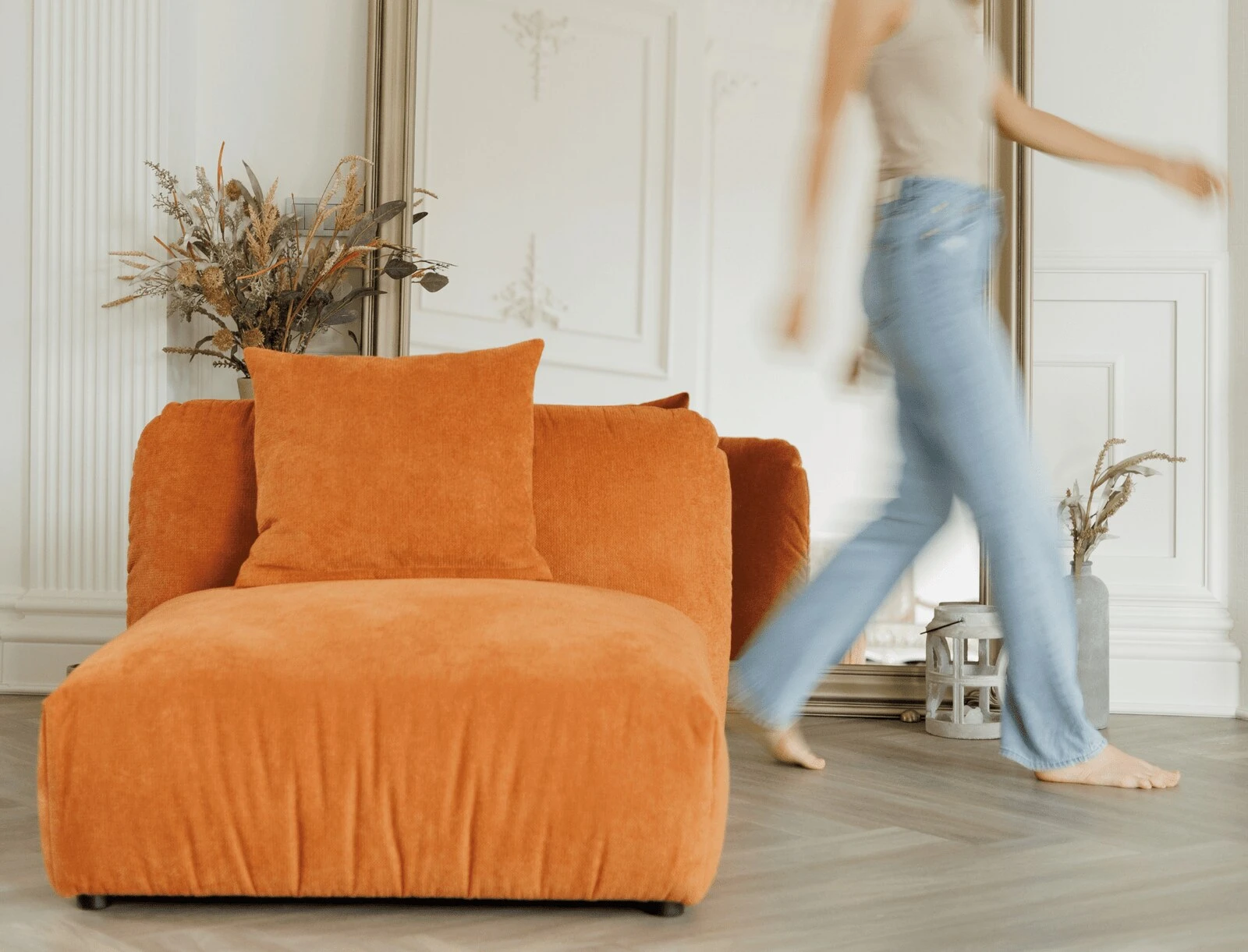 Rust corduroy Tesa armchair with dried floral, a model walking past in blue jeans