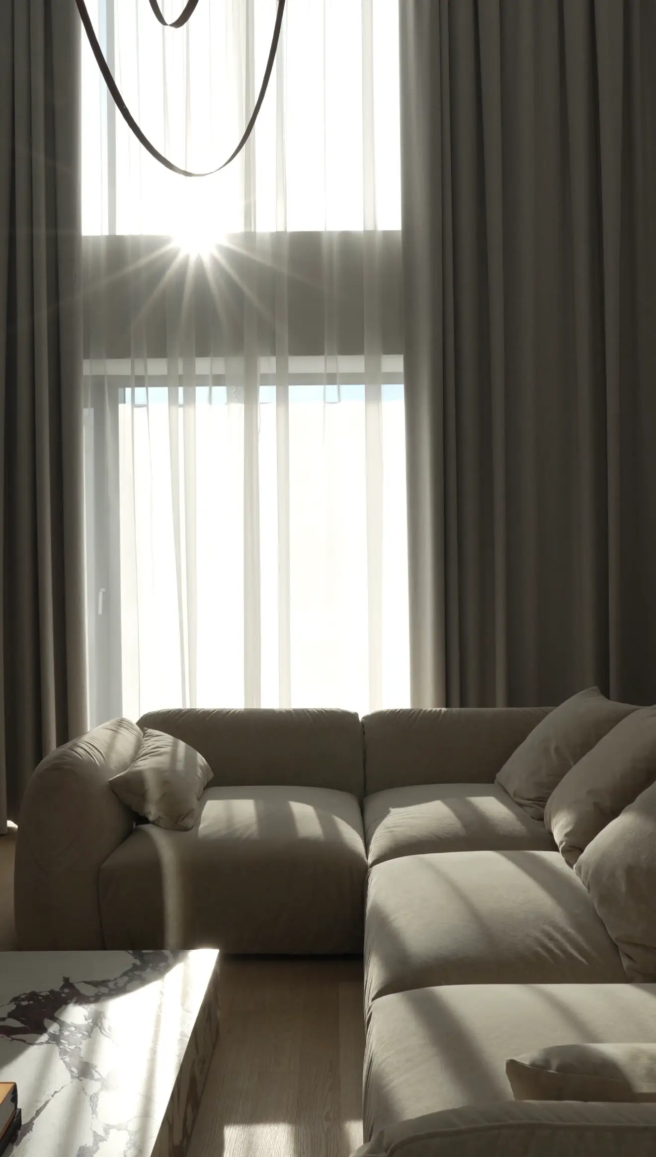 Double-height apartment with cream Tesa silhouetted against sun-burst flare through the curtain