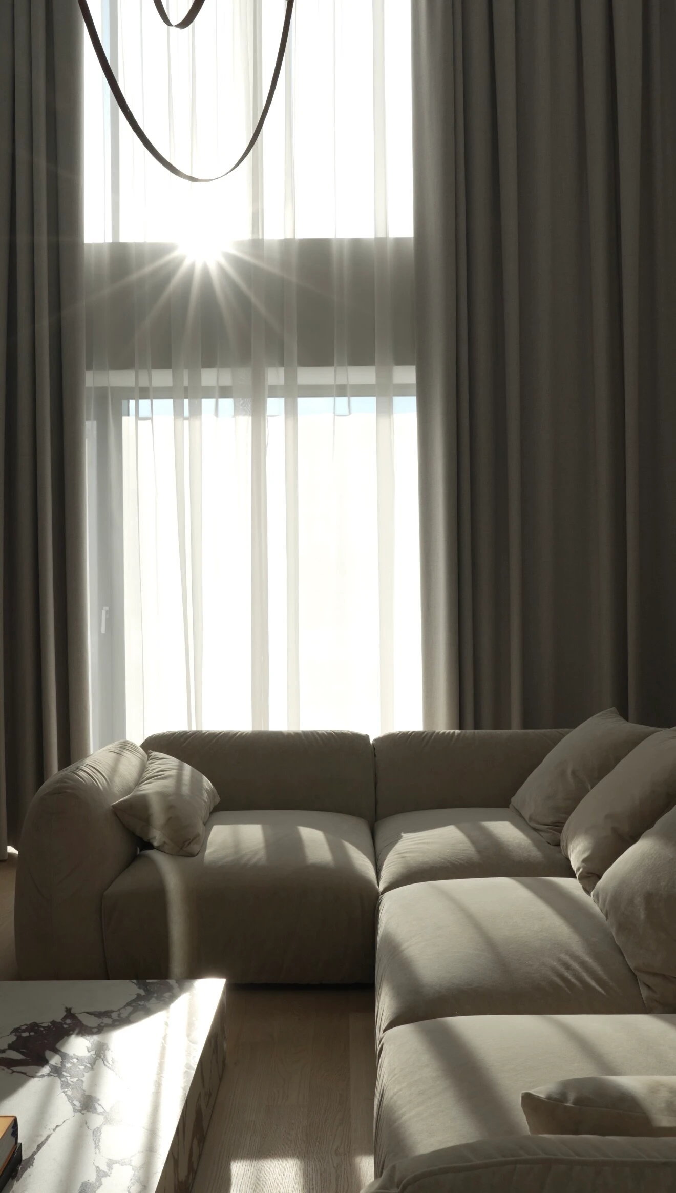 Double-height apartment with cream Tesa silhouetted against sun-burst flare through the curtain