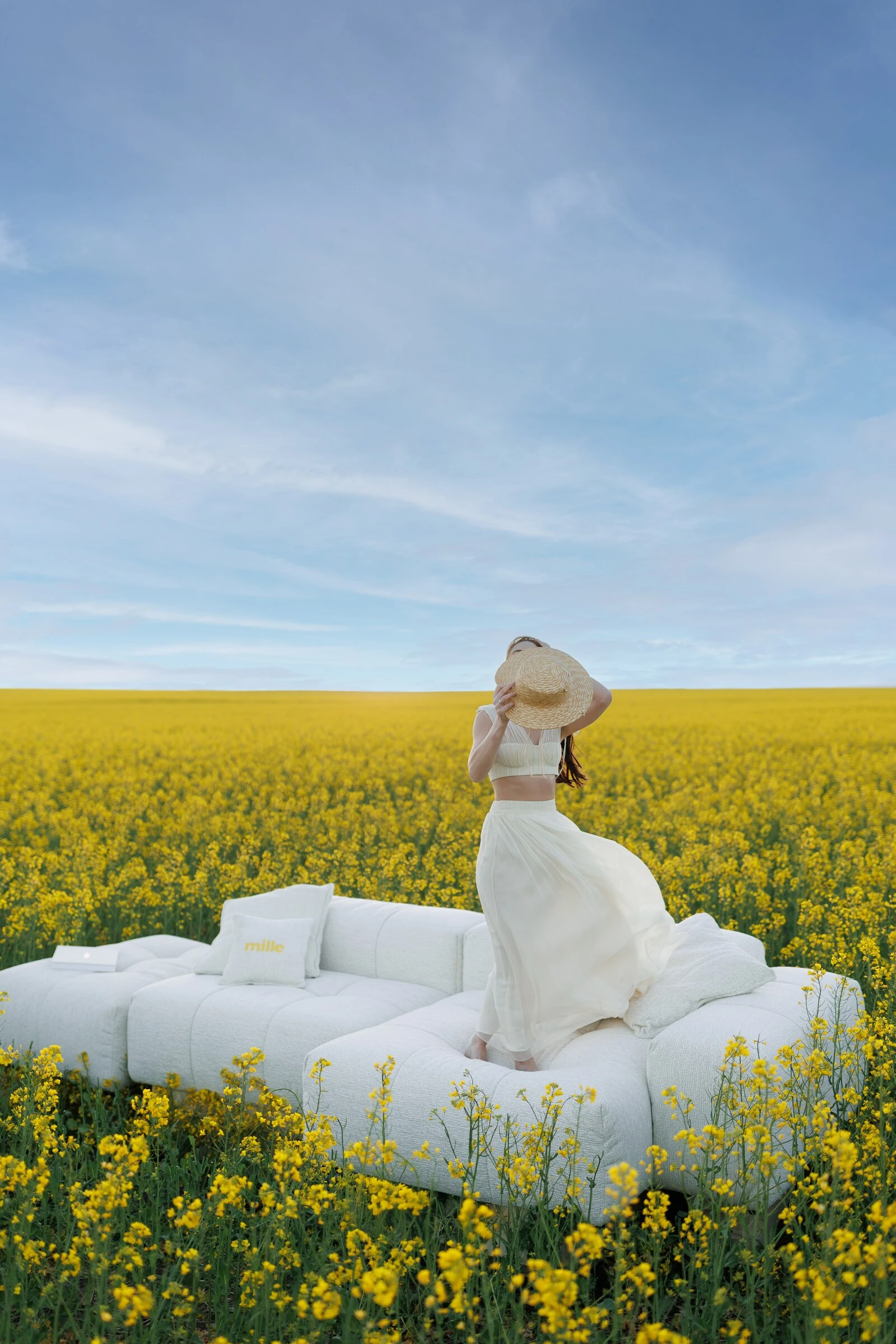 Woman in white with a straw hat seated on a cream Nami in a yellow canola field