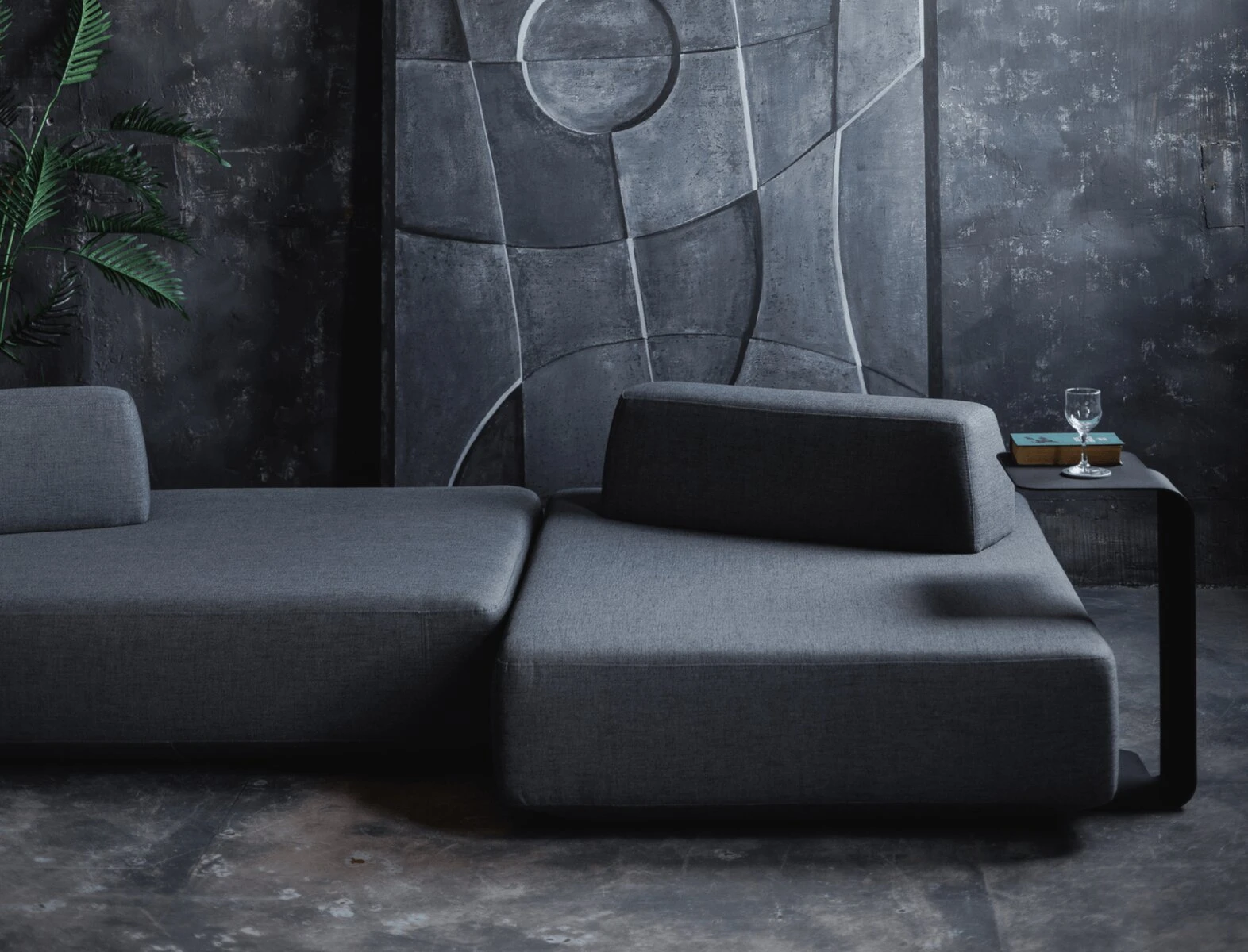 Charcoal Deseda in a dark concrete room with a tall industrial window and a leaning art panel