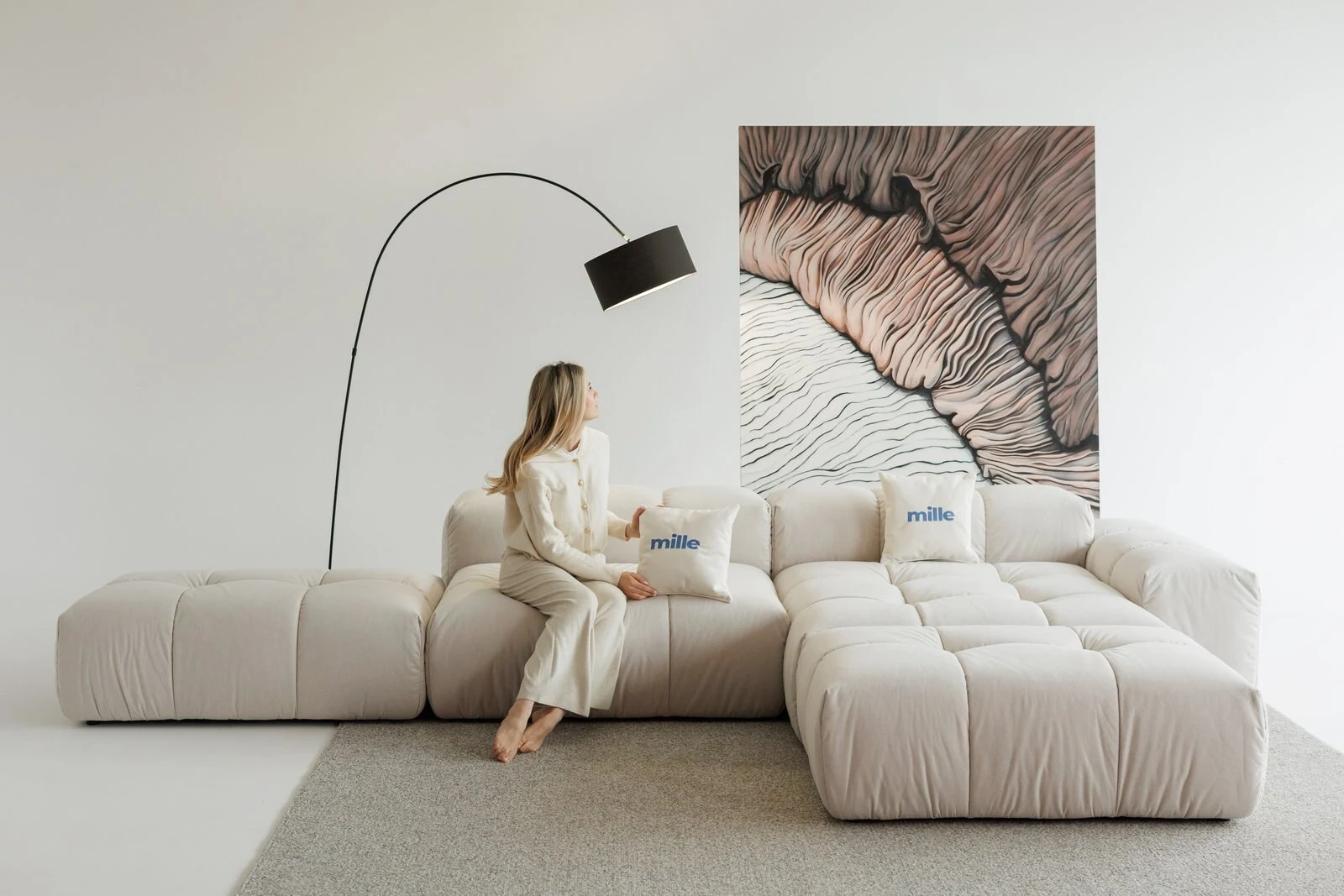 Woman seated on a cream Nami holding a Mille pillow with the wave panel behind