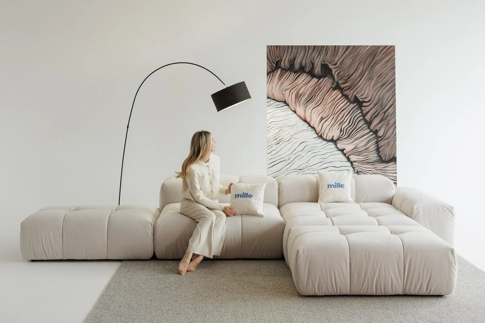Woman seated on a cream Nami holding a Mille pillow with the wave panel behind