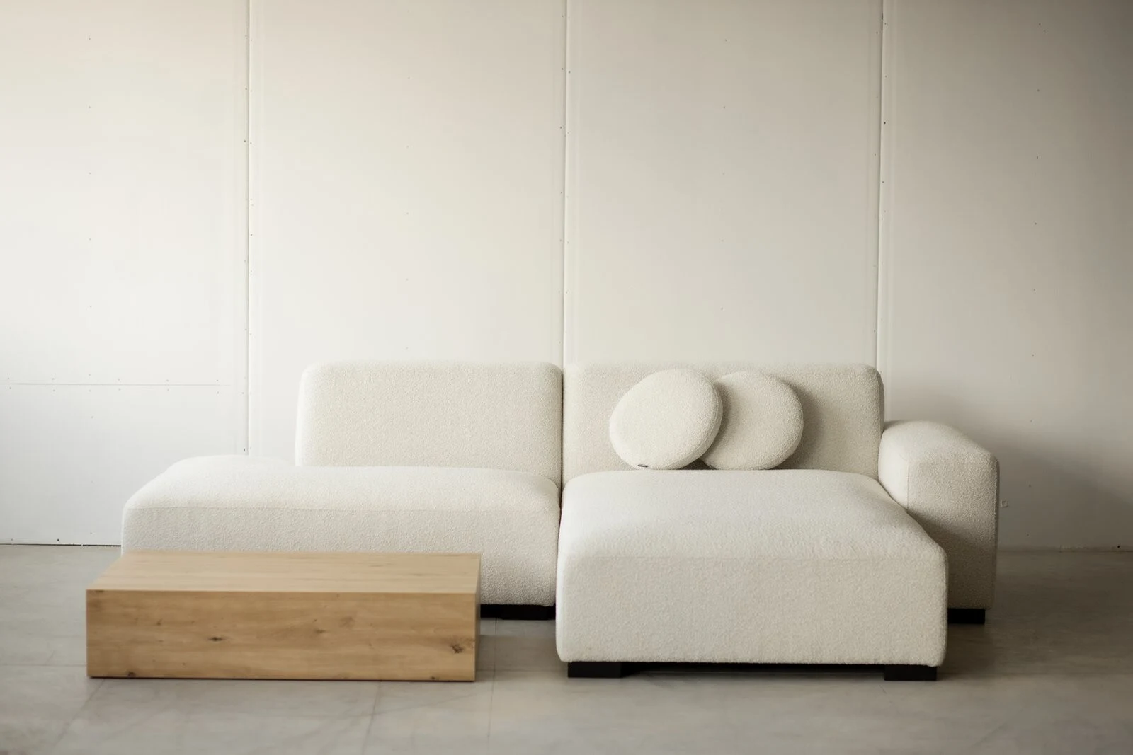 Cream boucle Kingston sectional in a white panel studio with an oak coffee table