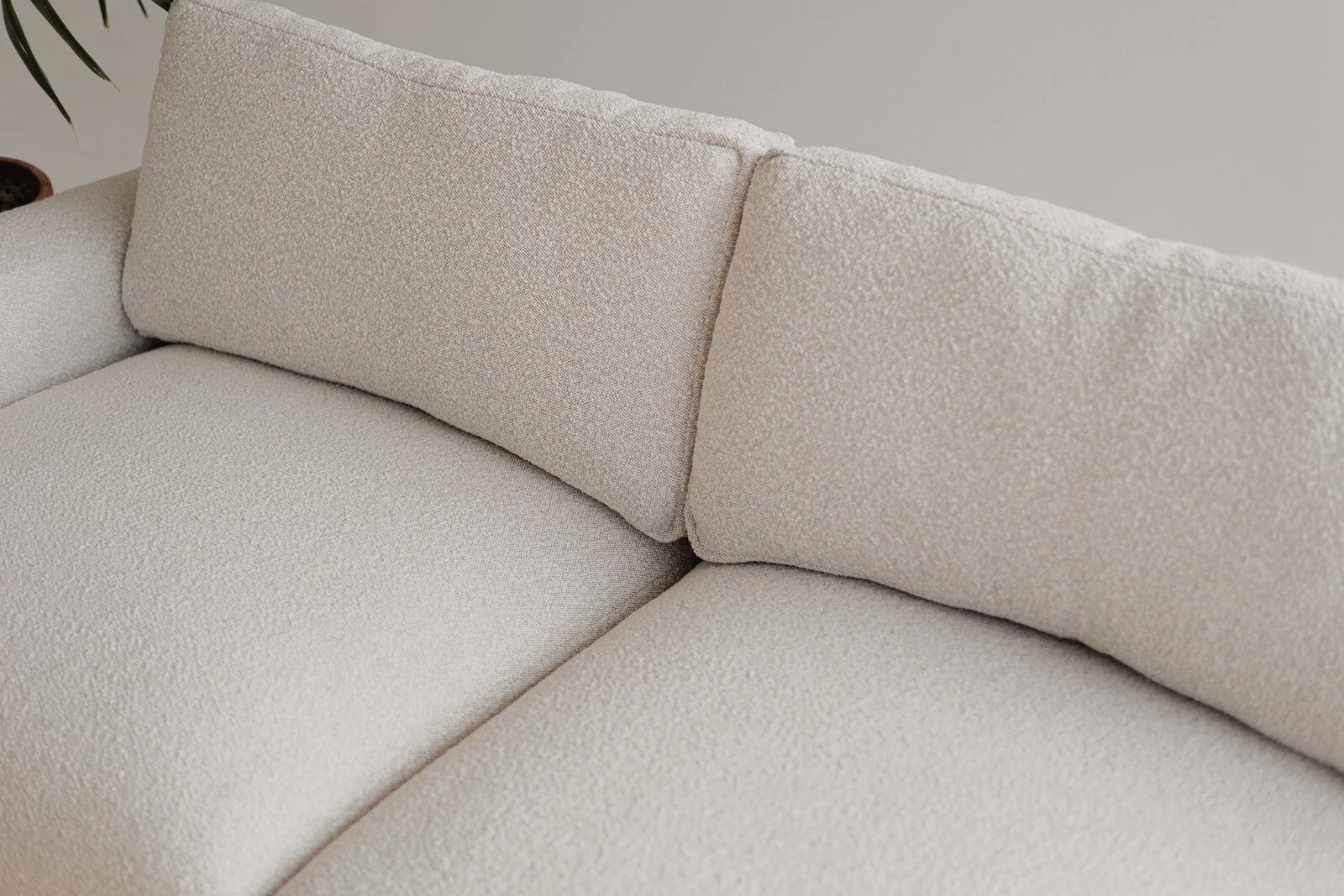 Cream boucle Palermo sectional in a sunny studio with industrial grid windows and a potted palm