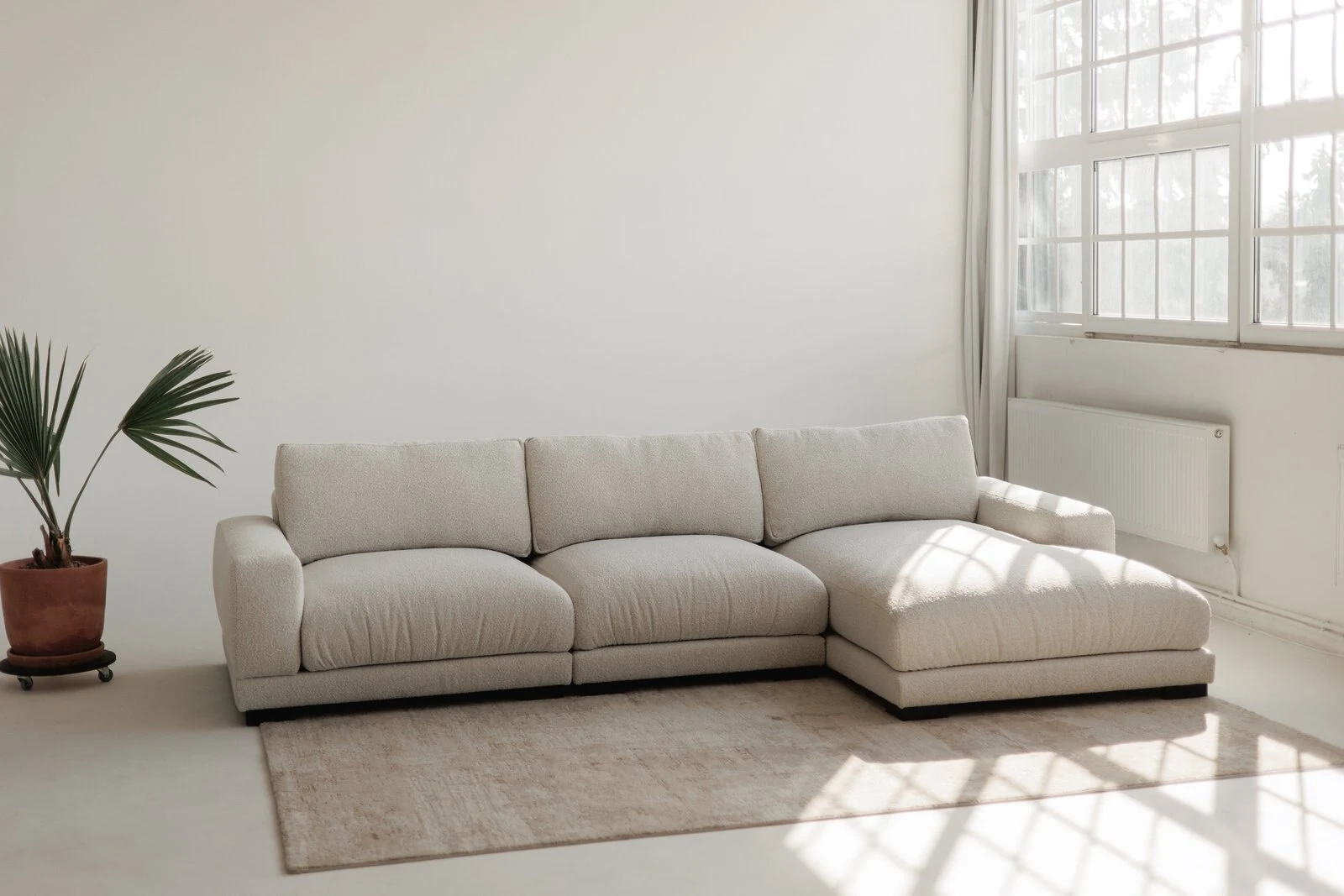 Cream Palermo sectional in a sunny studio with industrial grid windows and oak rug