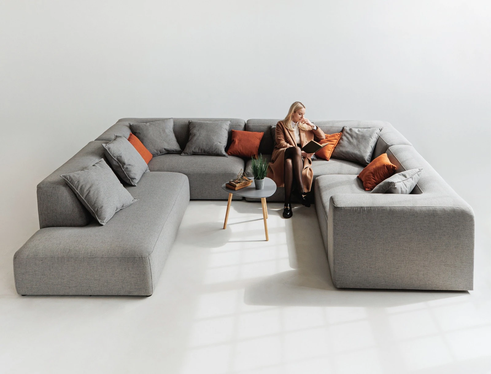 Grey Kingston U-shape with a model seated and reading, beside a marble side table