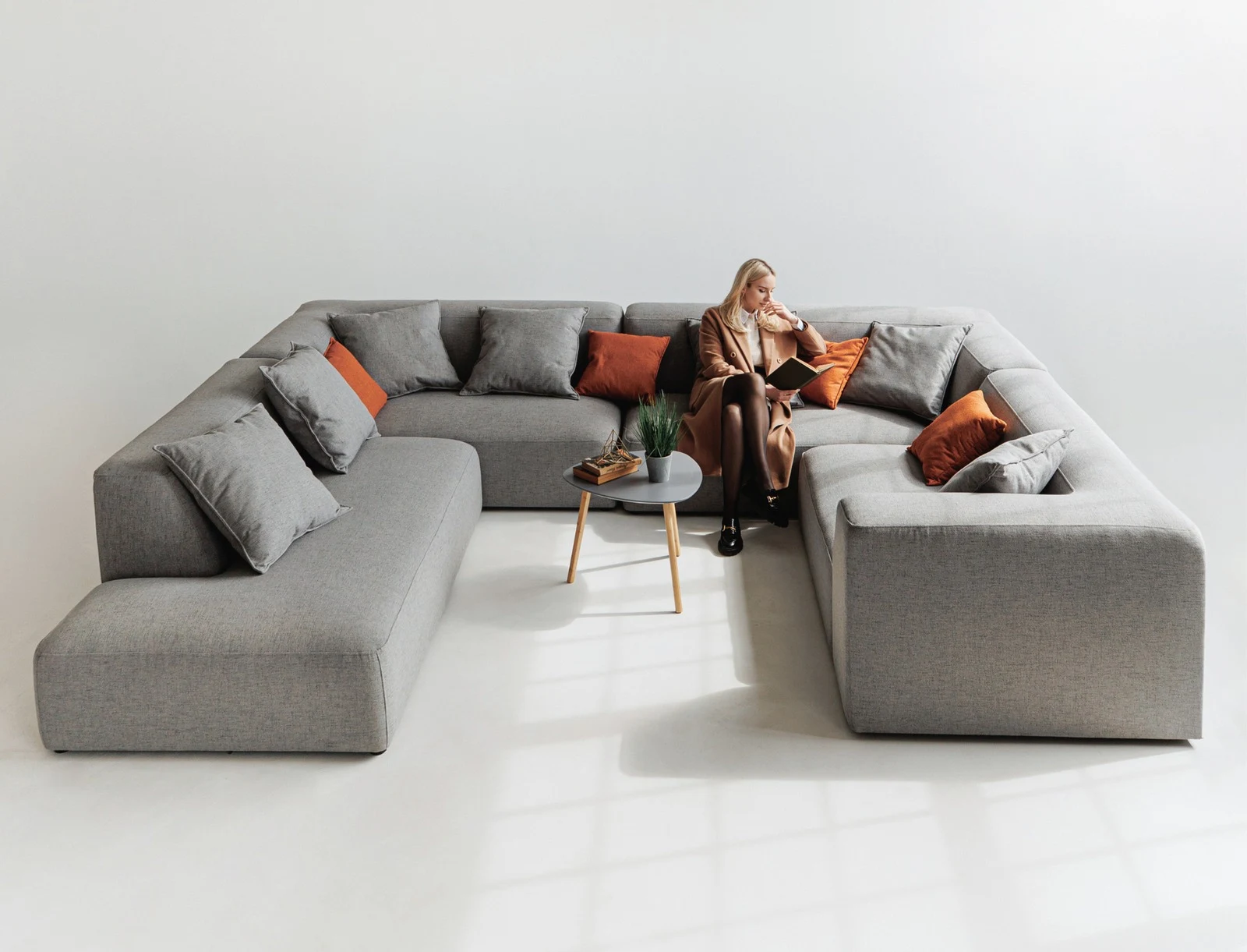 Grey Kingston U-shape with a model seated and reading, beside a marble side table