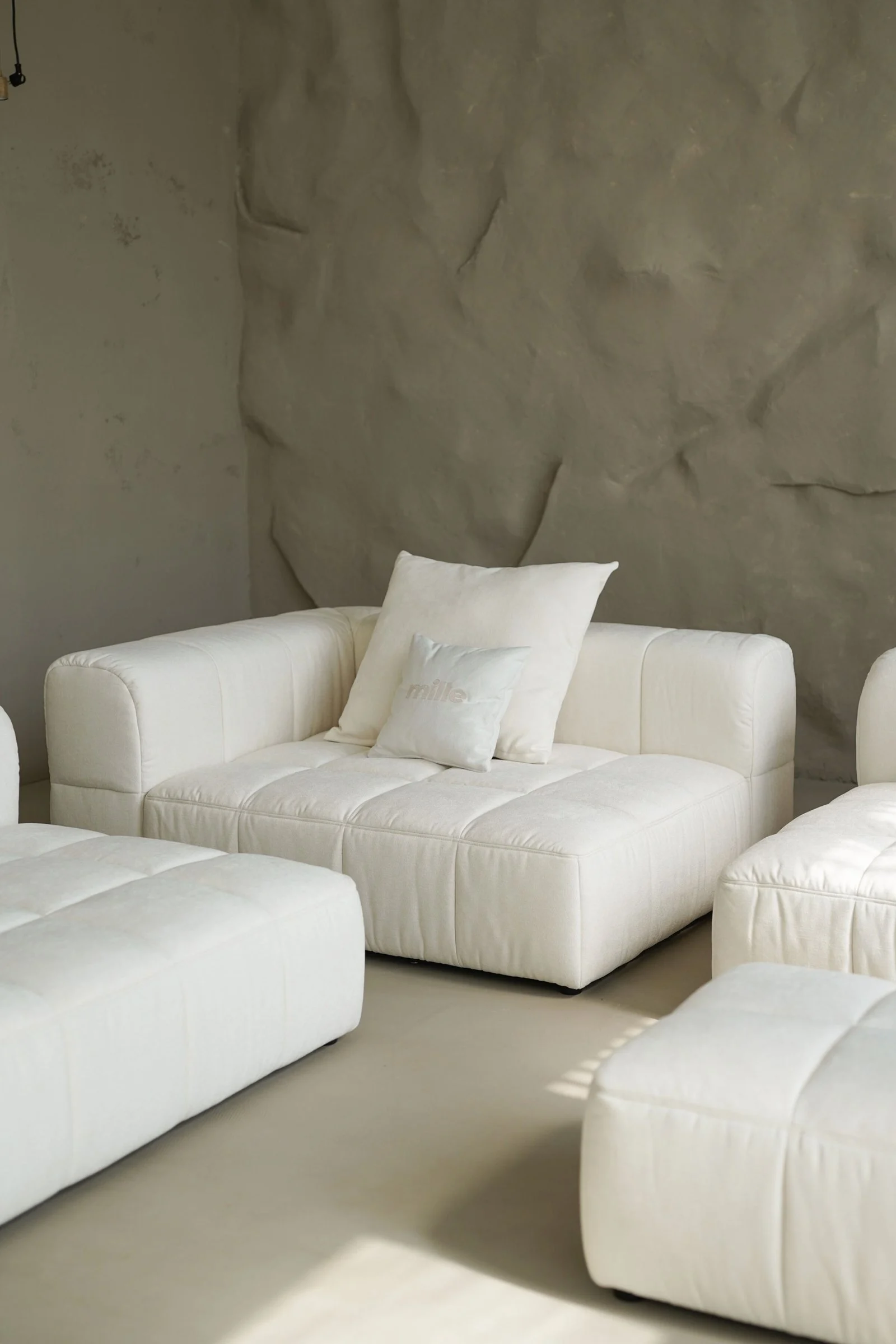 Cream tufted Soft modular sofa in a Mediterranean villa with a sheer rope curtain and golden sun-stripes on the cushions