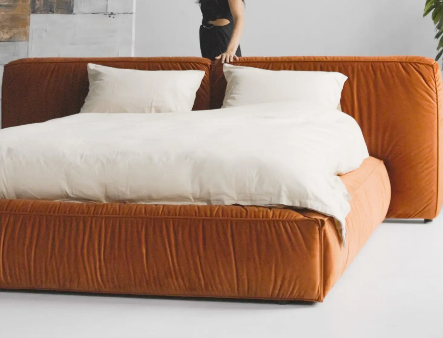 Burnt-orange velvet Palermo in a high-ceilinged loft with industrial windows, model in a black dress seated on the bed