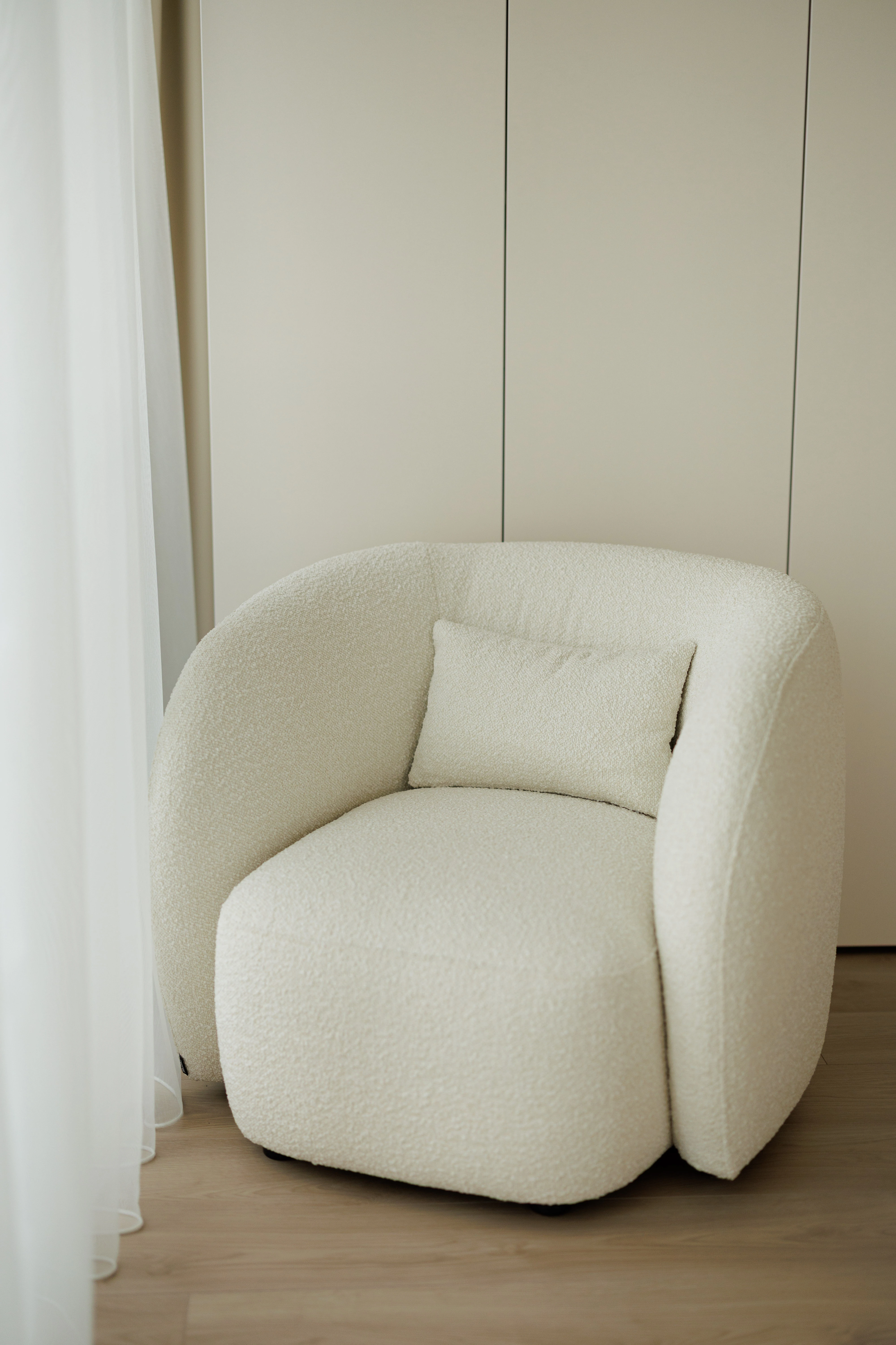 Cream boucle Nuba armchair in an apartment by a sheer white curtain