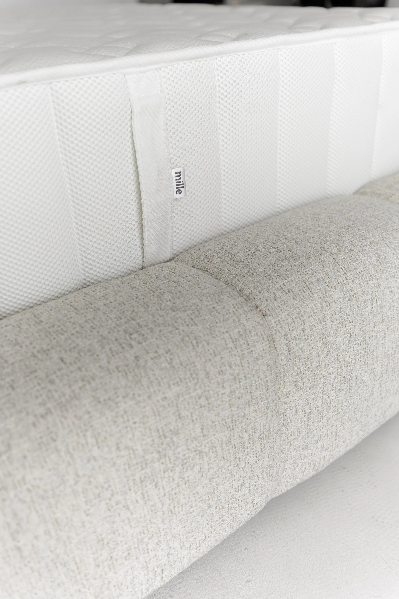 Close detail of a Mille-branded mattress edge resting on the Nao's channelled base
