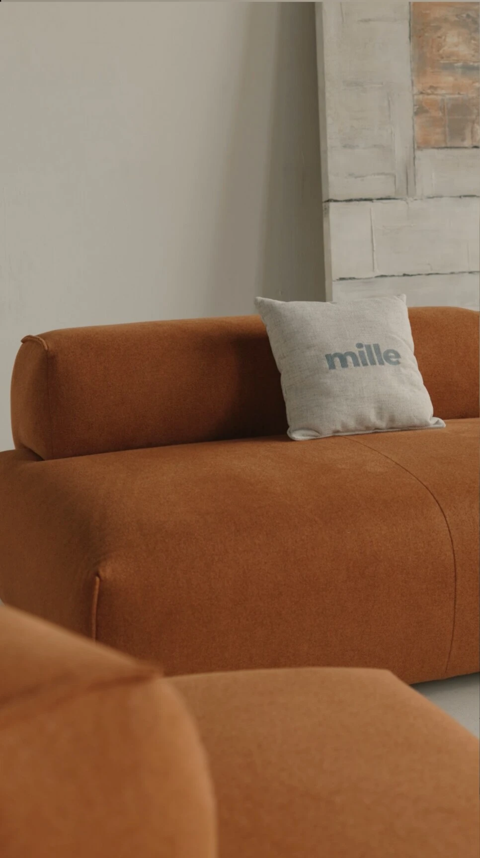 Close detail of the rust Nissa with a Mille pillow against an abstract art panel