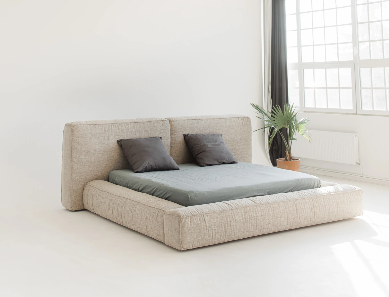 Sand-fabric Palermo in a bright minimal studio with a plant by the window and two grey pillows on the bed