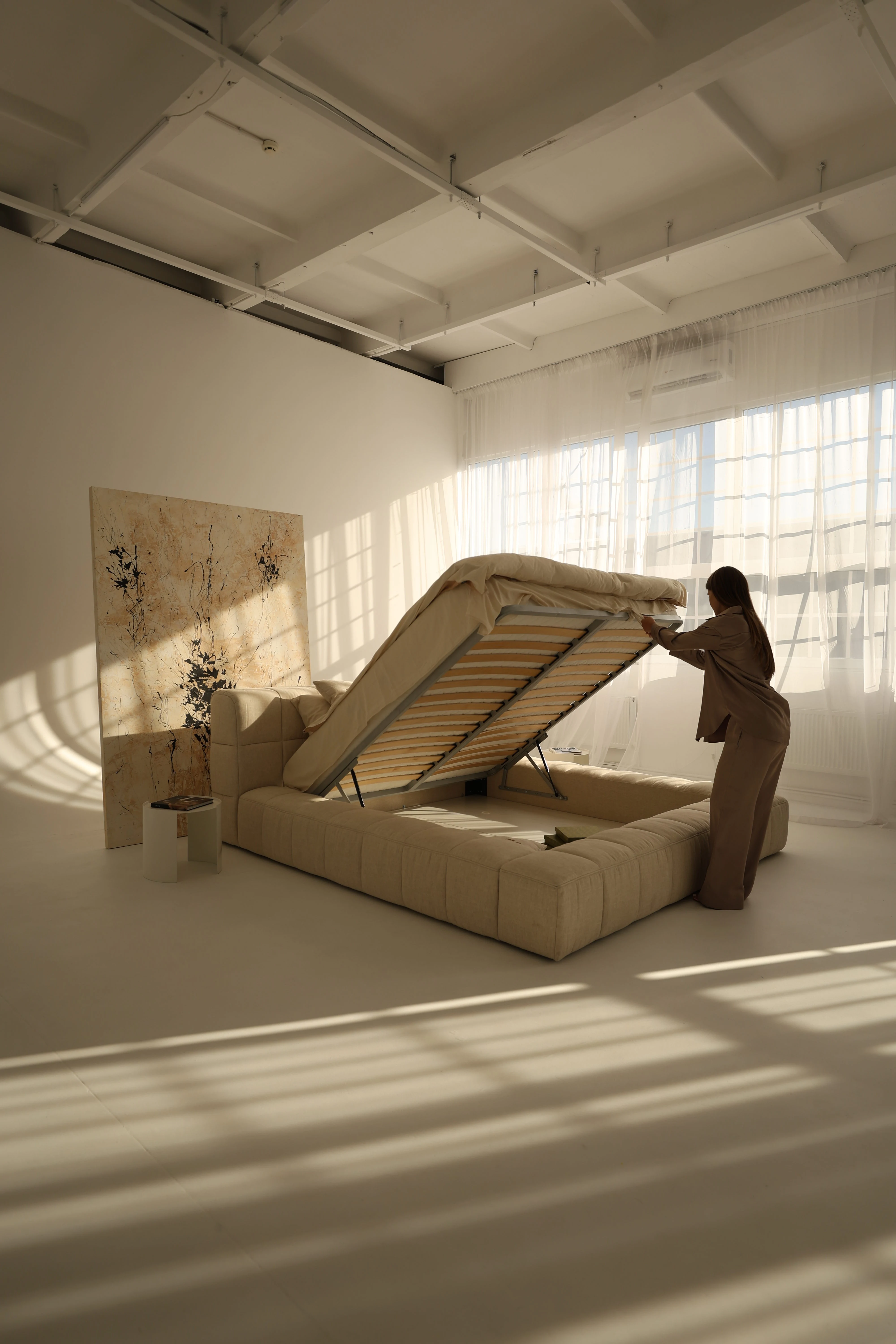 The Nao gas-lift base raised at 90 degrees, slatted wood platform visible, storage well underneath, model standing alongside